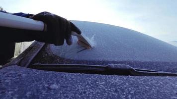 Mann, der das Auto im Winter nach Schneefall morgens mit der Bürste putzt. 4k Zeitlupenaufnahmen