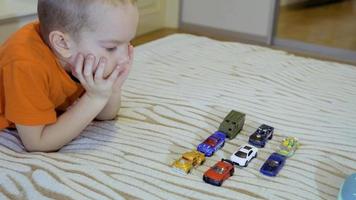 menino de cinco anos jogando carros modelo e mascando doces. vídeo 4k video