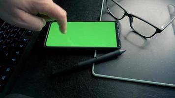 Man using mobile phone at his working place with the light on monitor. 4k video footage with green screen smartphone