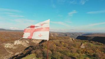 vista estática de la antigua bandera georgiana ondeando en cámara lenta con las ruinas históricas del edificio del pueblo de samshvilde video