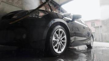 hombre lavando auto en el garaje de lavado de autos con una mujer parada esperando en la reflexión sobre el auto lateral video