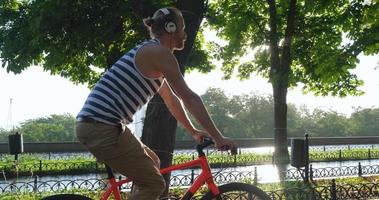 jonge knappe man met kleurrijke fiets en koptelefoon luistert naar muziek en rijdt door de zomerstraten video