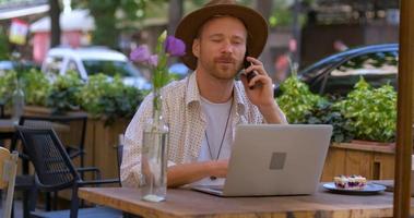 joven hipster guapo con laptop al aire libre en el café, trabajo independiente barbudo en el café de la calle video