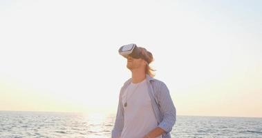 Portrait of young handsome male on the beach wearing virtual reality glasses, beautiful sunrise on the background video