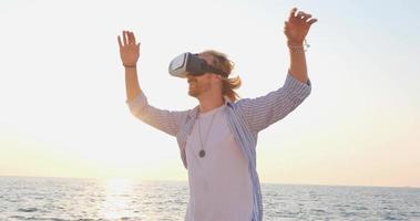 portret van een jonge knappe man op het strand met een virtual reality-bril, prachtige zonsopgang op de achtergrond video