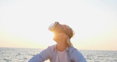 Portrait of young handsome male on the beach wearing virtual reality glasses, beautiful sunrise on the background video