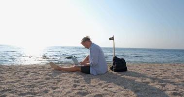 jonge knappe man op het zomerstrand werkt met laptop tijdens zonsopgang video