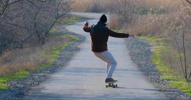 jovem passeio masculino no skate longboard na estrada rural em dia ensolarado video
