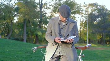 joven hipster masculino con bicicleta retro lee un libro en el parque de otoño video