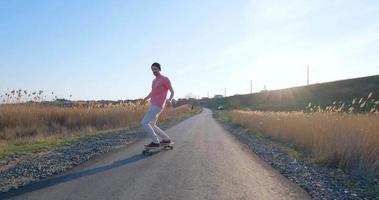 jeune homme ride sur planche à roulettes longboard sur la route de campagne en journée ensoleillée video