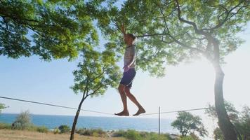 Athlete walking in slackline in the park with sea and blue sky on background video