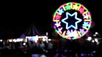 Blurred illuminated decorative lighting on ferris wheel and carousel with many people in night festival fair area