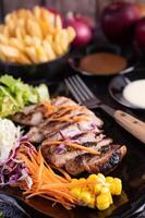 Pork steak with bread, carrots, cauliflower, lettuce and corn on a black plate. photo