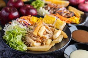 Chicken steak with bread, carrots, cauliflower, turnips, and corn on a black plate. photo