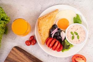 el desayuno consta de pan, huevo frito, aderezo para ensaladas, uvas negras, tomates y rodajas.