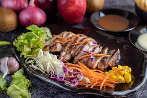 Pork steak with bread, carrots, cauliflower, lettuce and corn on a black plate. photo