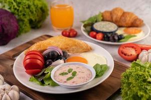 el desayuno consta de pan, huevo frito, aderezo para ensaladas, uvas negras, tomates.