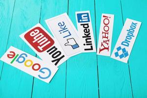 kiev, ucrania - 10 de marzo de 2017. colección de logotipos de redes sociales populares impresos en papel youtube, google, yahoo, linkedin, dropbox y similares sobre fondo de madera azul. copie el espacio foto