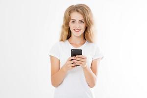 Young beautiful woman in t shirt using her smartphone isolated on white background. Sexy blond girl chating with friend or shopping online. Copy space photo