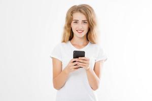 Young beautiful woman in t shirt using her smartphone isolated on white background. Sexy blond girl chating with friend or shopping online. Copy space photo