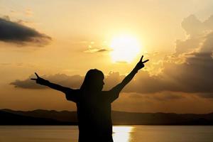 Silhouette of woman standing arms raised in the sunset. Strong female with open arms silhouette in sunrise against sun flare. Carefree person living a free life. Success freedom happy life concept.