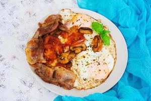 Fried eggs with bacon, tomatoes and mushrooms on white background. Top view photo