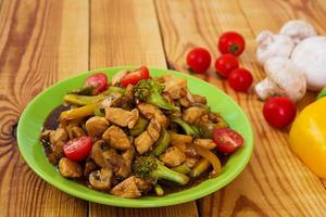 Stir fry chicken, zucchini and broccoli on wooden background photo