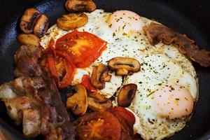 Fried eggs with bacon, tomatoes and mushrooms on white background. Top view photo