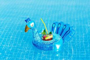 mojito de cóctel fresco en un juguete inflable de pavo real azul en la piscina. concepto de vacaciones.