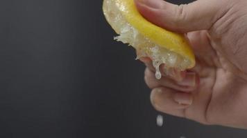 mão espremendo metade de limão com limão cair em fundo preto.