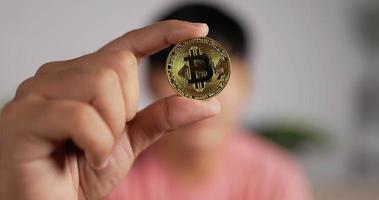 primo piano di un uomo asiatico che tiene bitcoin. l'uomo sfocato mostra la moneta d'oro sulla fotocamera. concetto finanziario e di investimento in criptovaluta.