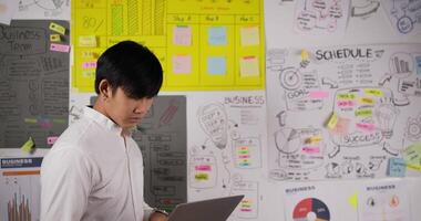 Front view of Businessman checking laptop and chart while standing in office. Young man make a strategy, meeting, briefing. Show on whiteboard with sticky notes in a modern office. video