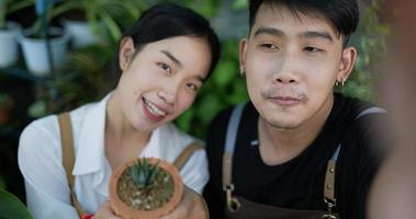 retrato de um feliz jardineiro jovem casal asiático vendendo on-line nas mídias sociais e olhando para a câmera no jardim. selfie de homem e mulher com telefone celular. verdura em casa, venda online e hobby.
