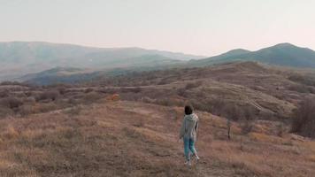 vista lateral feminina caucasiana andando no campo Prado cercado na natureza do outono. sonhar acordado e bem-estar do conceito de mulher solo