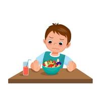 niño quisquilloso que se niega a comer mostrando la mano empujando el tazón de frutas y verduras