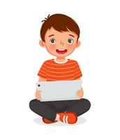 Cute little boy sitting on floor using digital tablet touching screen browsing internet, doing homework, and playing games. Kids and electronic gadget devices concept for children vector