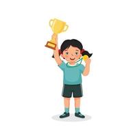 Happy cute little girl holding up a gold cup trophy and medal celebrating winning sport competition