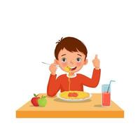 lindo niño comiendo deliciosos espaguetis usando un tenedor mostrando gestos con el pulgar hacia arriba vector