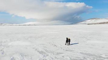 Panning aerial view Female woman with young boy kid walks holding hands on white frozen lake winter landscape background