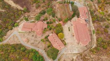 Aerial view down to Shio - Mgvime monastery with tourists walking and around. Orthodox monasteries buildings architectural plan video