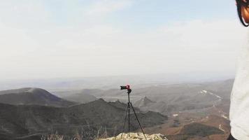 jeune femme caucasienne regarde à travers l'appareil photo professionnel du viseur avec panorama de fond de montagnes. photographe de voyage sur le concept de terrain. video