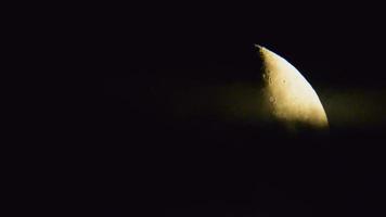 Zoom in view yellow lunar moon setting behind clouds in black background. Layers in atmosphere.