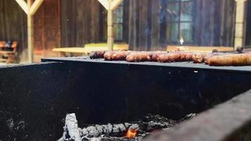 close-up saborosas salsichas chiando no fogo de churrasco grelhando em um piquenique de verão na vila rural de férias. grelhar comida, churrasco, churrasco video