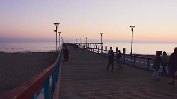 Palanga, Lithuania , 2021 - People walking at dawn on wooden famous Palanga pier. Famous summer travel destination in Lithuania video