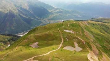 Aerial vie down to Koruldi lakes with gravel road and mountains panorama in summer