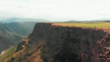 Aerial view of scenic valley landscape in Armenia with female tourist sit on cliff pose for photographs for social media. Travel outdoors in summer concept video