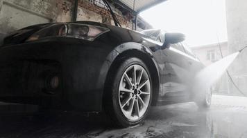 persoon start zwarte luxe auto met power jet spray voor vrouwelijke klant met gezichtsmasker op pandemie in car wash garage. video