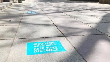 2. sinal azul pintado com título mantenha distância em inglês e georgiano no pavimento de asfalto de pedestres com pessoa andando nas proximidades. novos regulamentos e conceito de regras de segurança. tbilisi. Geórgia.