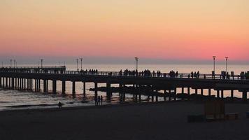 peatones con vista estática caminando por el puente del muelle de palanga después de la pintoresca puesta de sol sobre el famoso punto de referencia. vacaciones de vacaciones en lituania. video