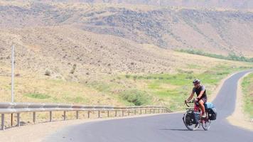 Static view caucasian male cycle solo on red bicycle uphill in extreme heat outdoors in scenic nature. Bicycle touring adventure lifestyle concept video